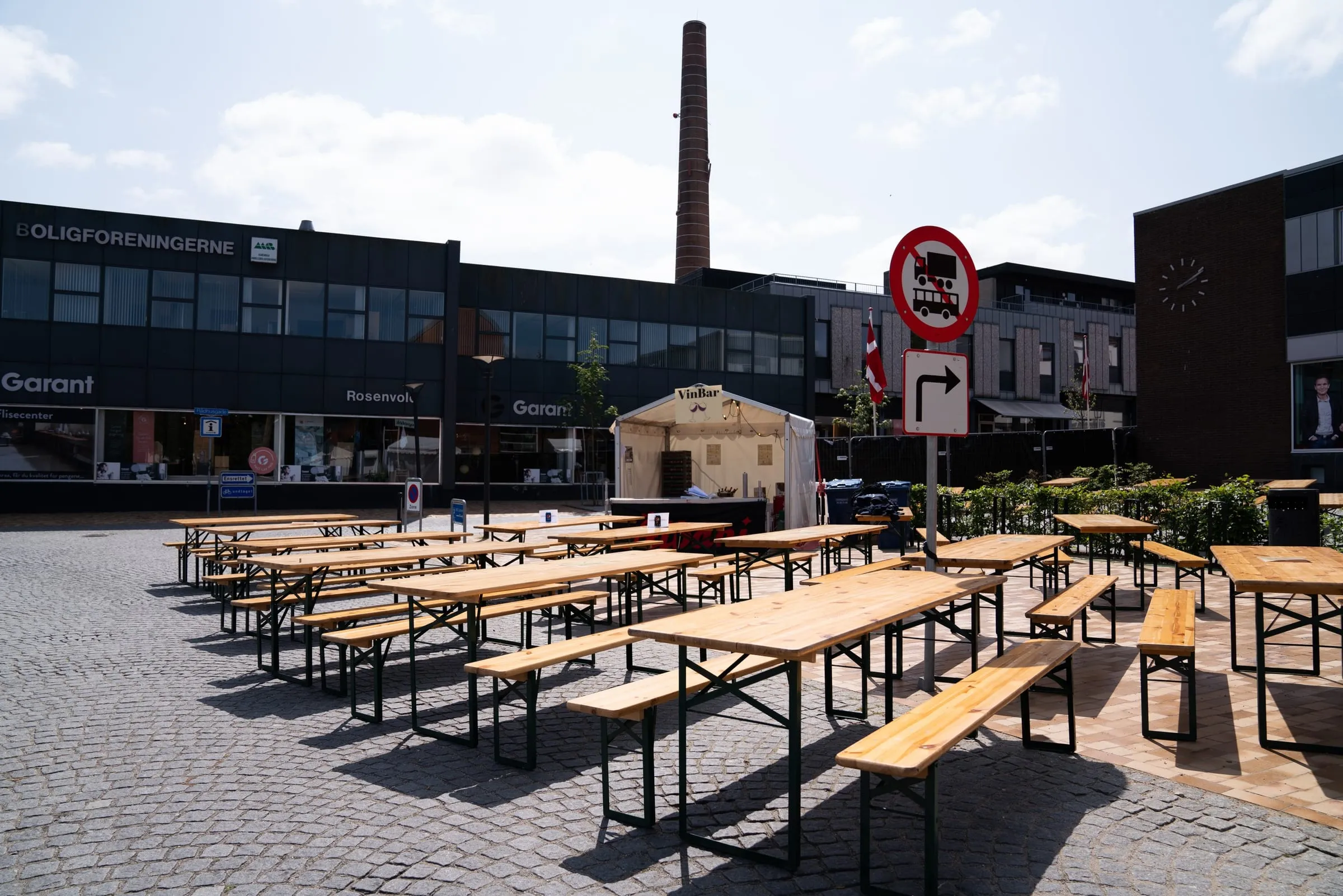 Tomme ølborde stillet op i lige rækker på pladsen, skorstenen bagved, timer før åbning