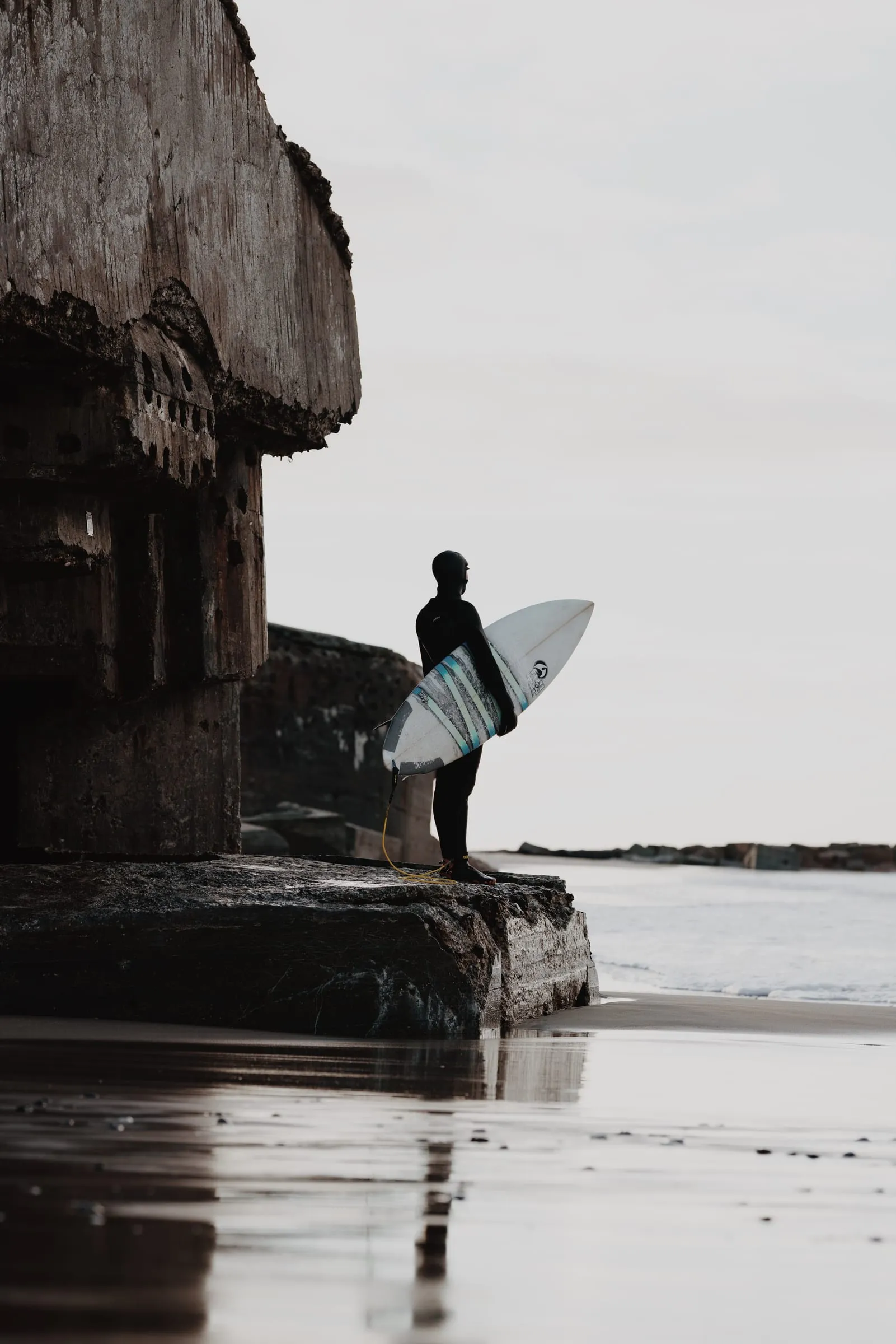 Surfer med brættet står på en sammenstyrtet bunker og kigger ud over havet