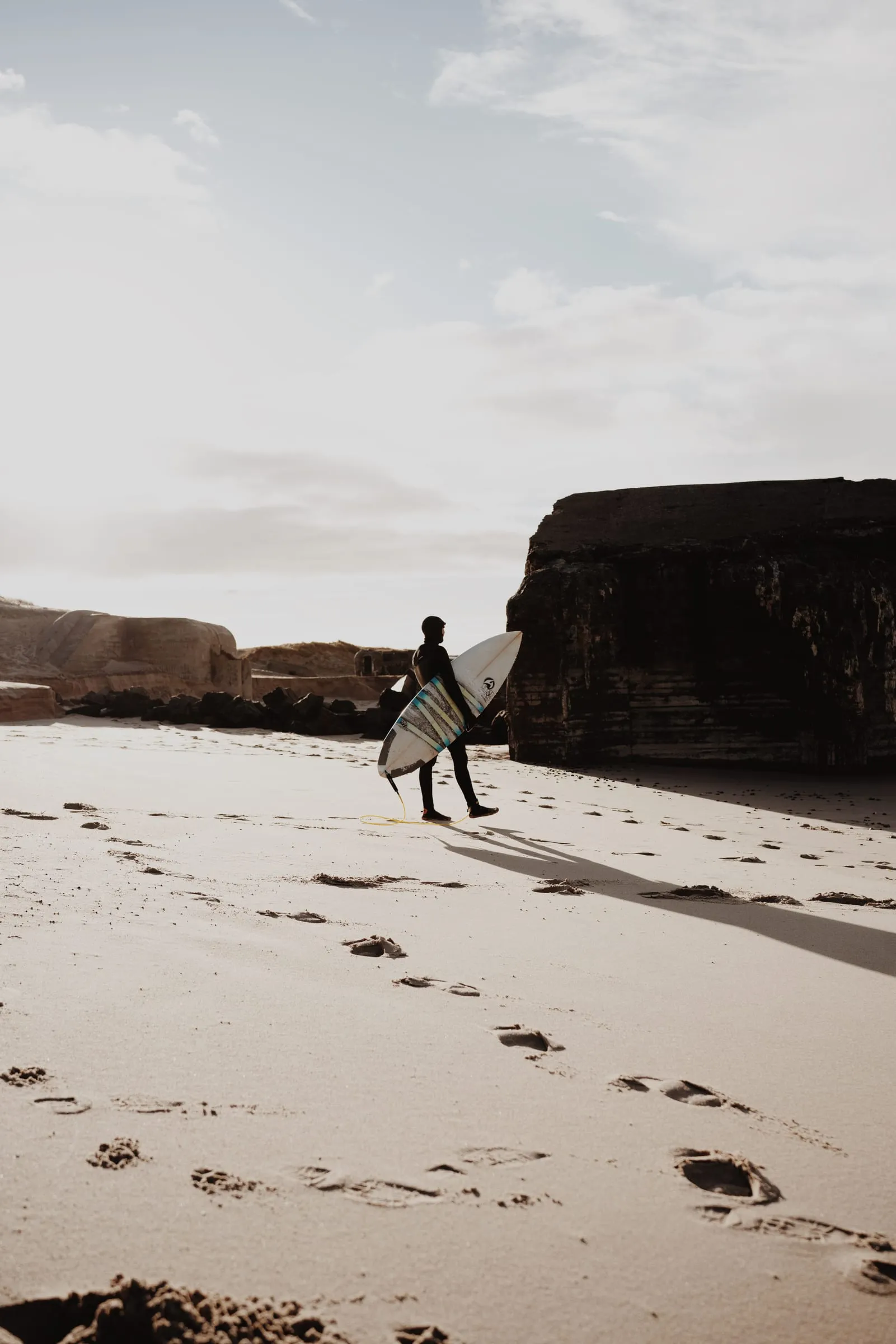 Surfer går over den brede strand mod bunkerne, fodspor på kryds i sandet
