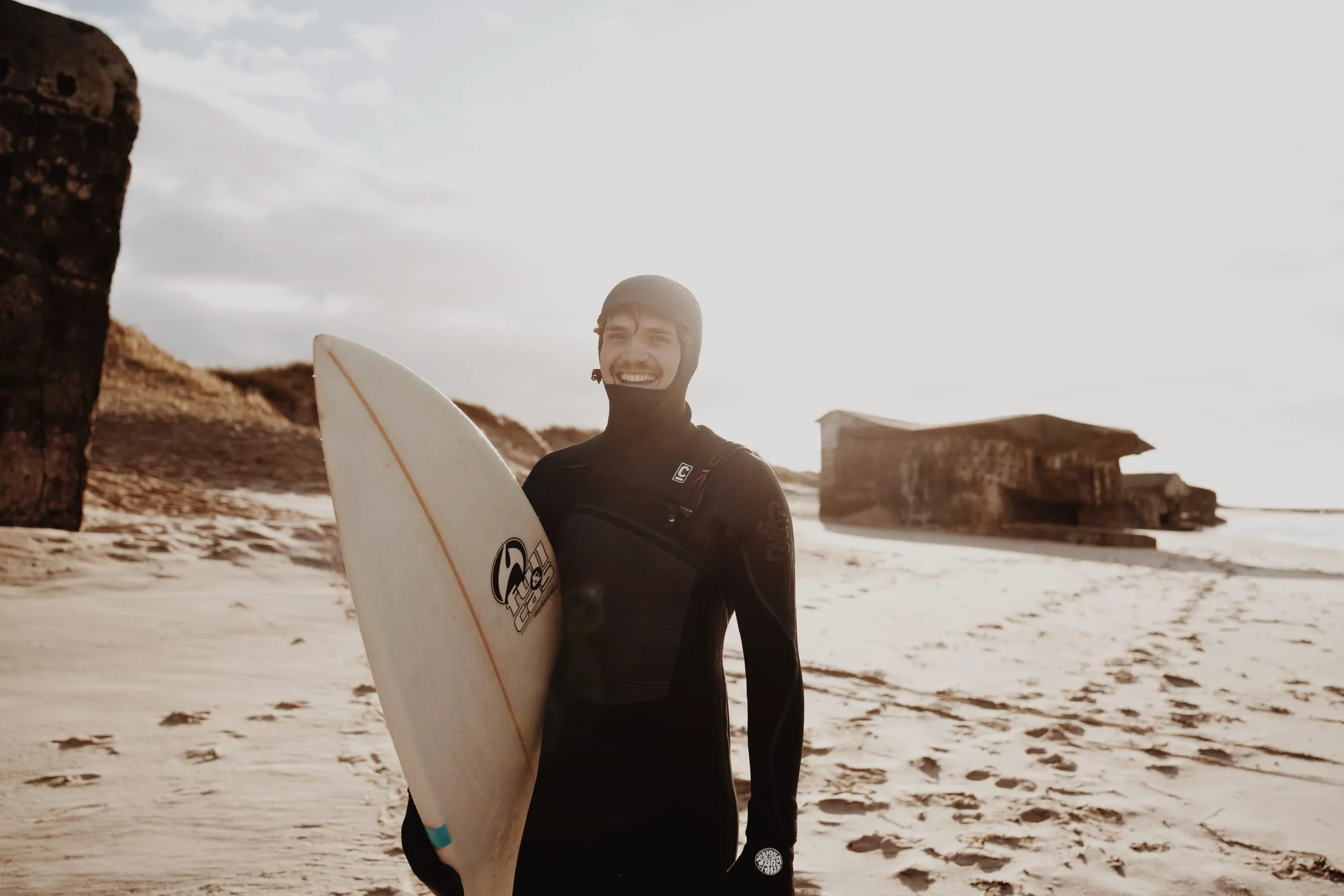 Surfer med brættet under armen på den brede strand, bunkeren til højre