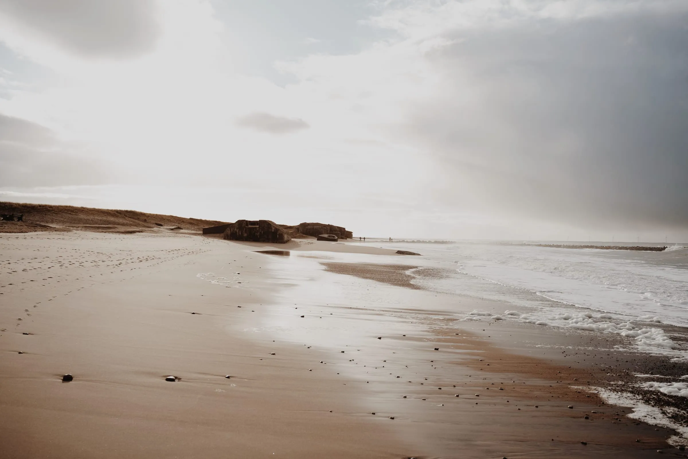 Tom strand i modlys med bunkerne i klitkanten og havet rullende ind fra højre