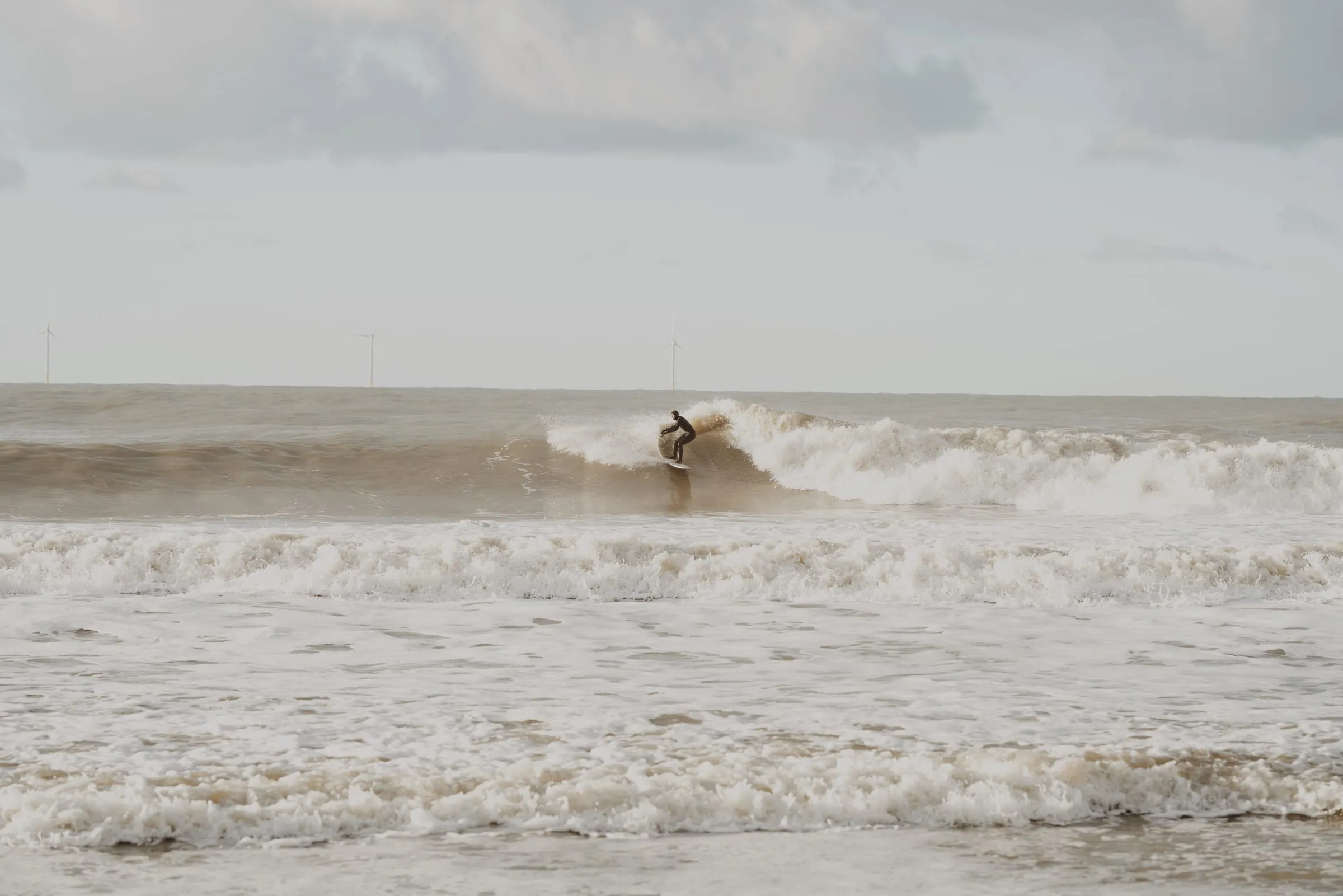 Surfer på en lille bølge langt ude, havvindmøller i horisonten