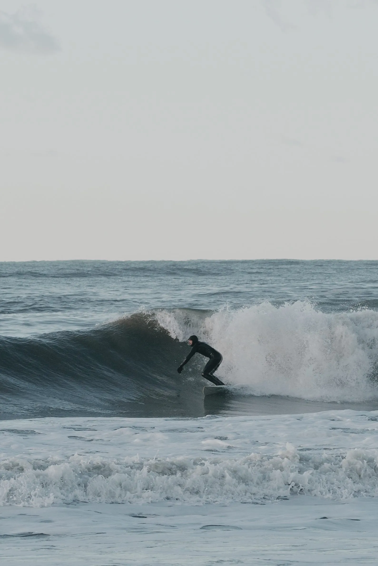 Surfer rider ned ad en bølge med hvid top i det grå hav