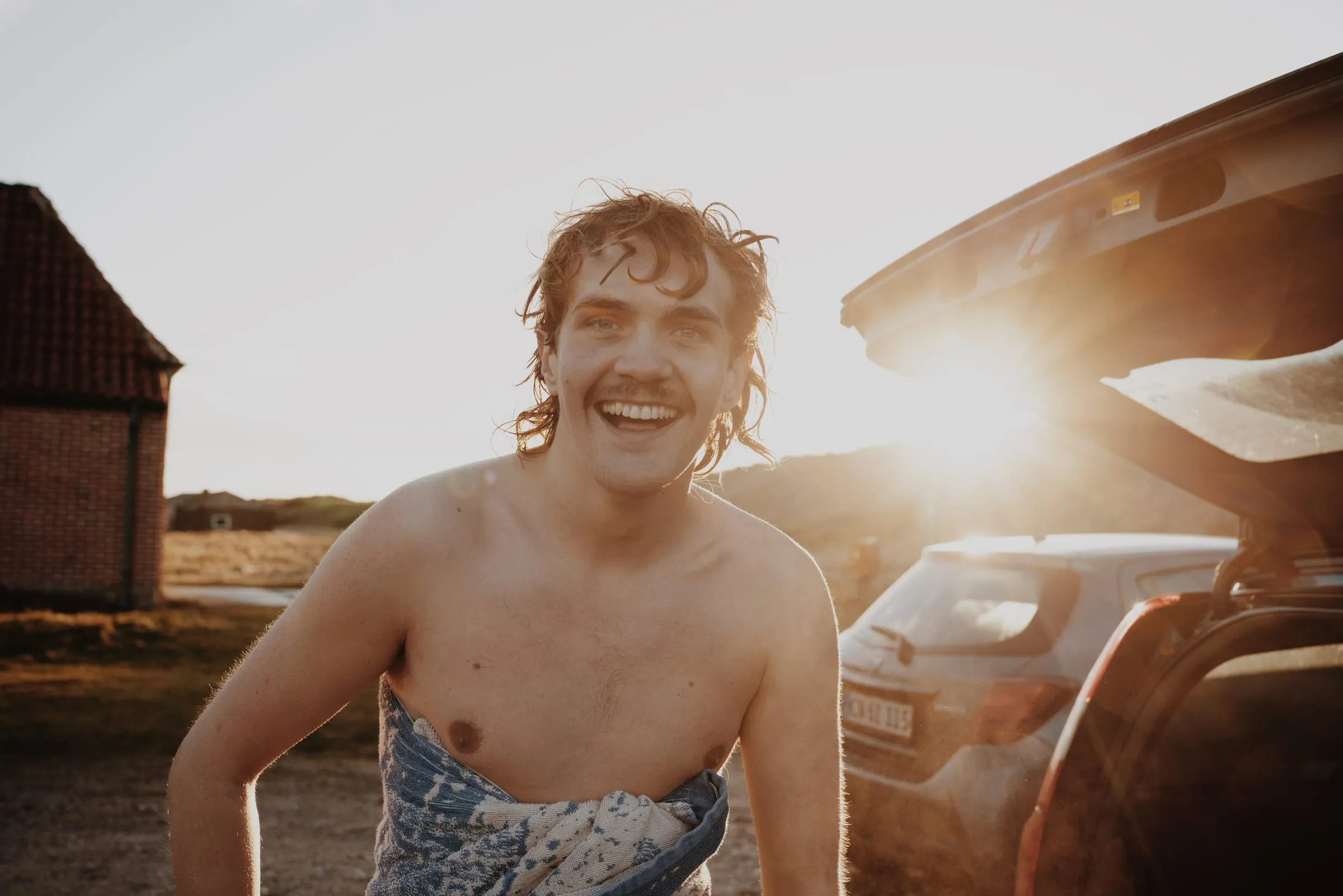 Surferen ler mod kameraet med håndklædet om livet i modlys