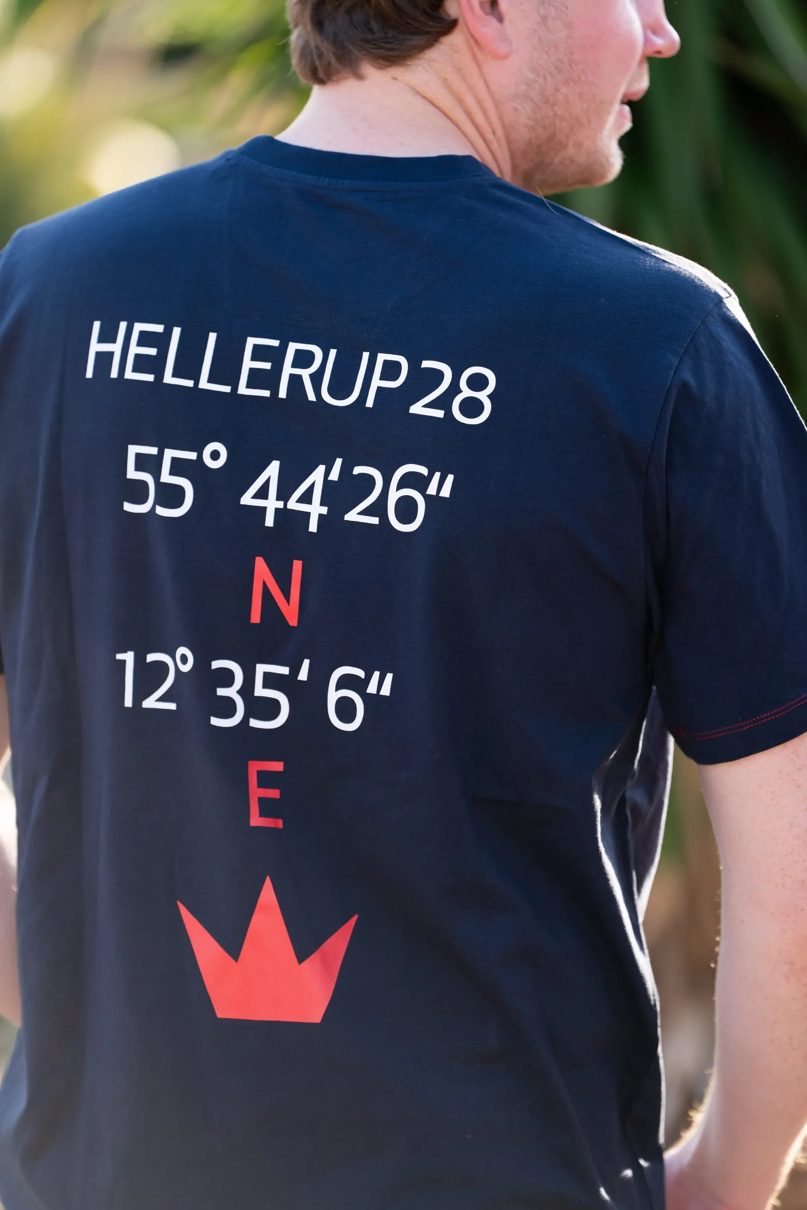 Ryggen af en navyblå T-shirt med Hellerup28-koordinater og rød krone