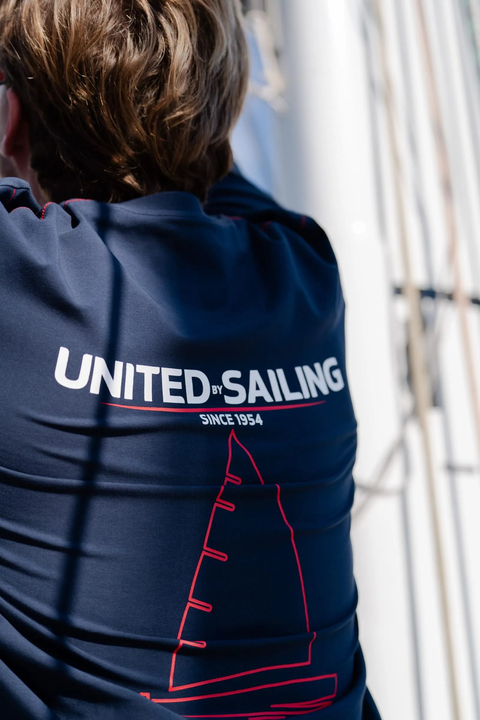 Ryggen af en navyblå trøje med United-Sailing-tryk foran riggen