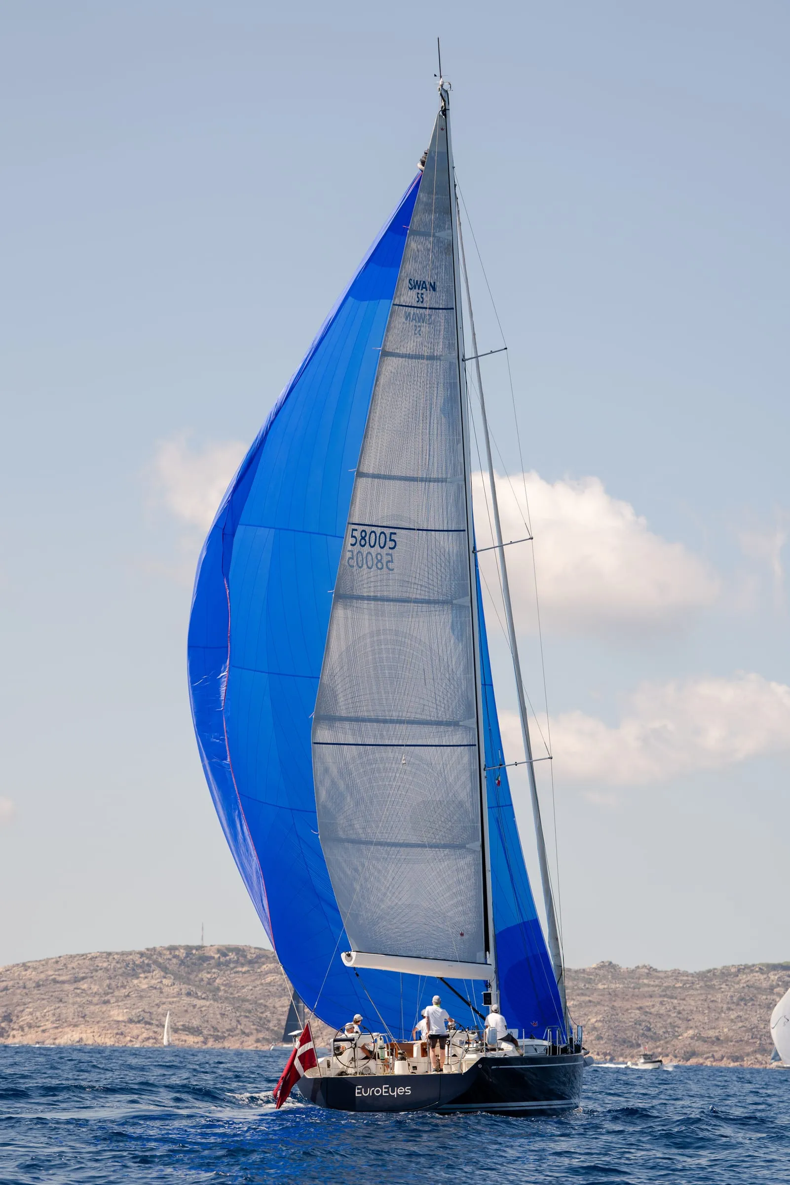 Yachten under blå spiler langs Sardiniens klippekyst